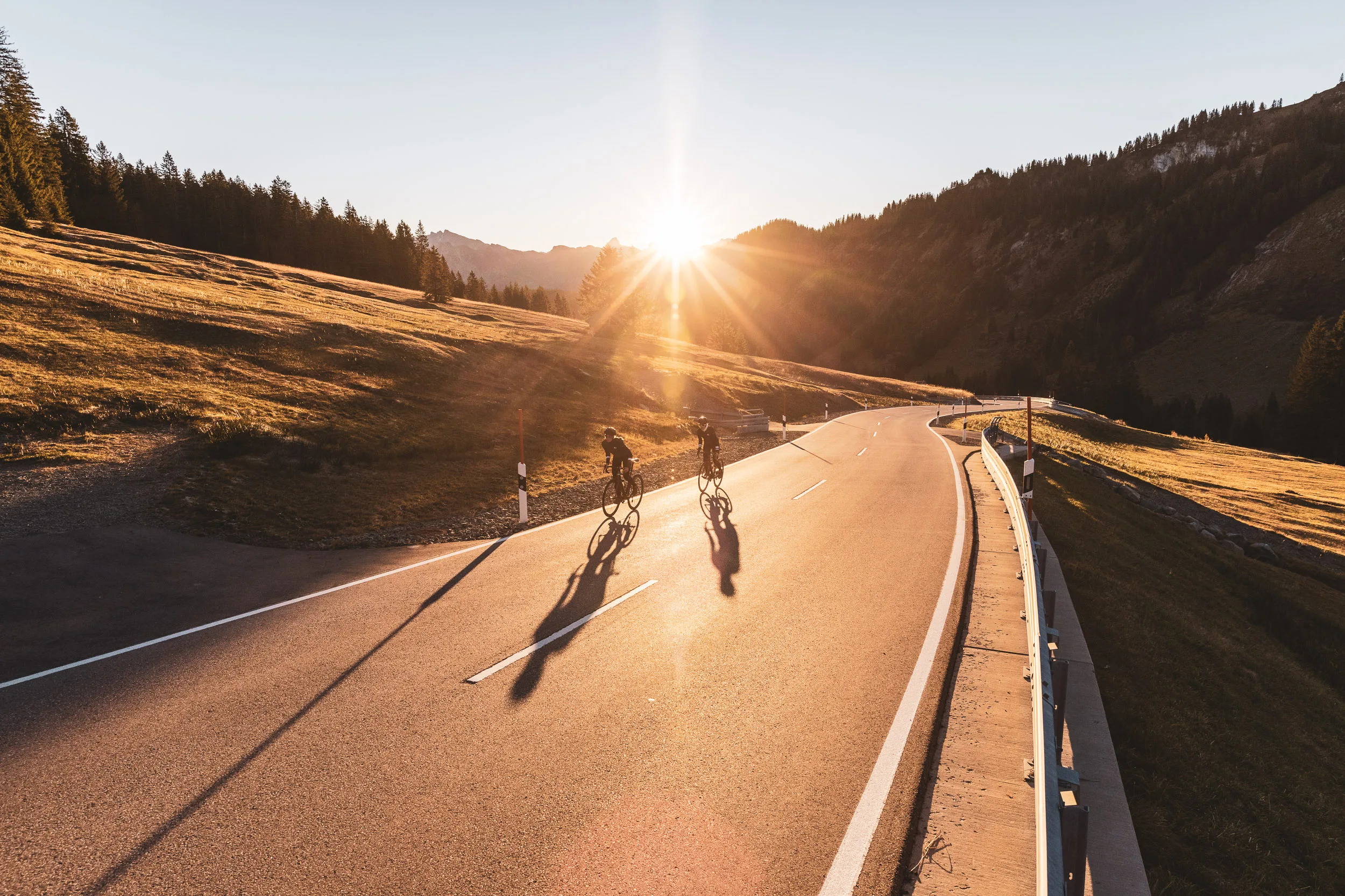 Luftaufnahme von zwei Rennradfahrerinnen auf der Passstraße im Abendlicht