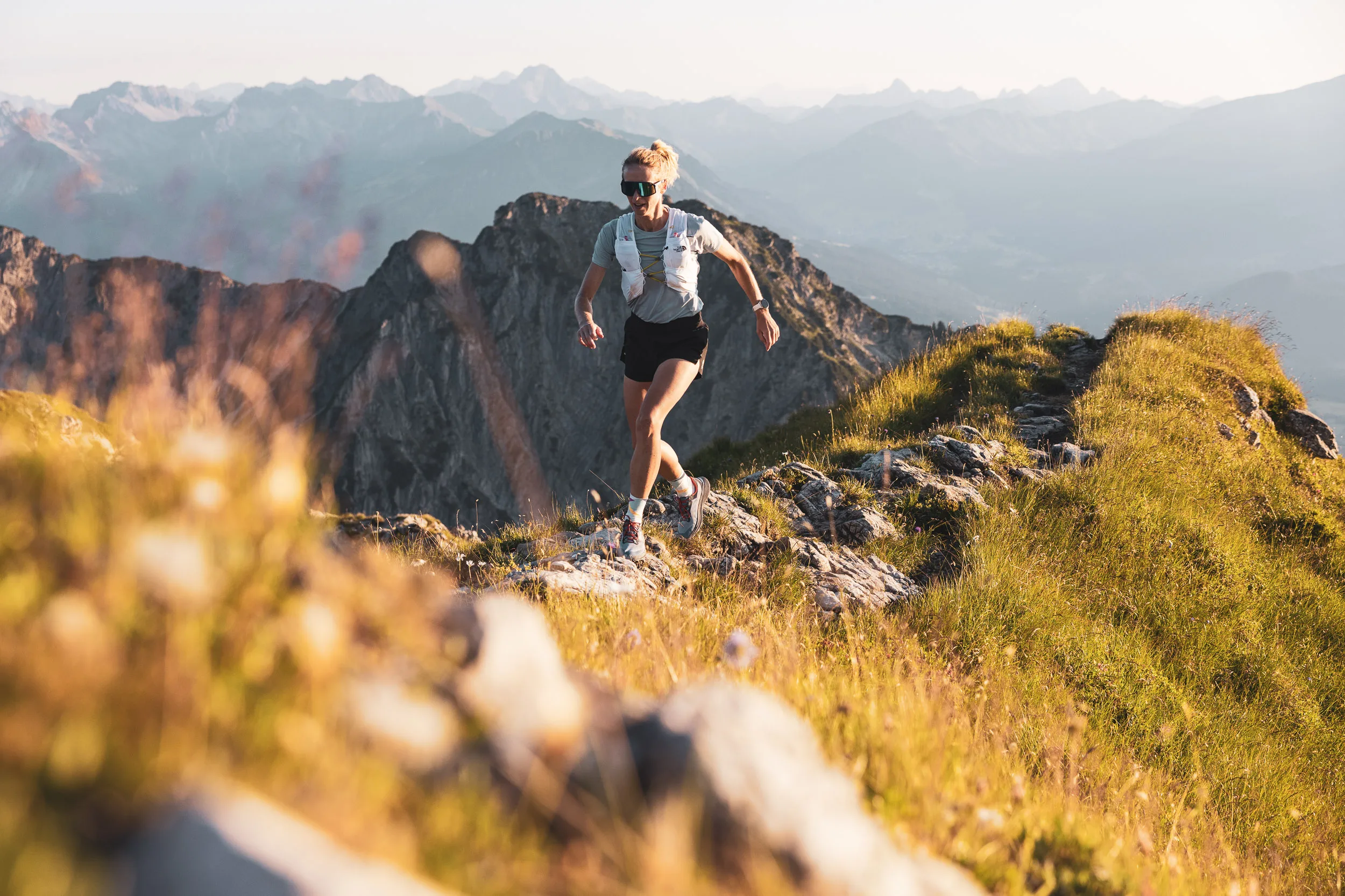 Trailrunnerin im Abendlicht auf einem felsigen Weg am Berggrat