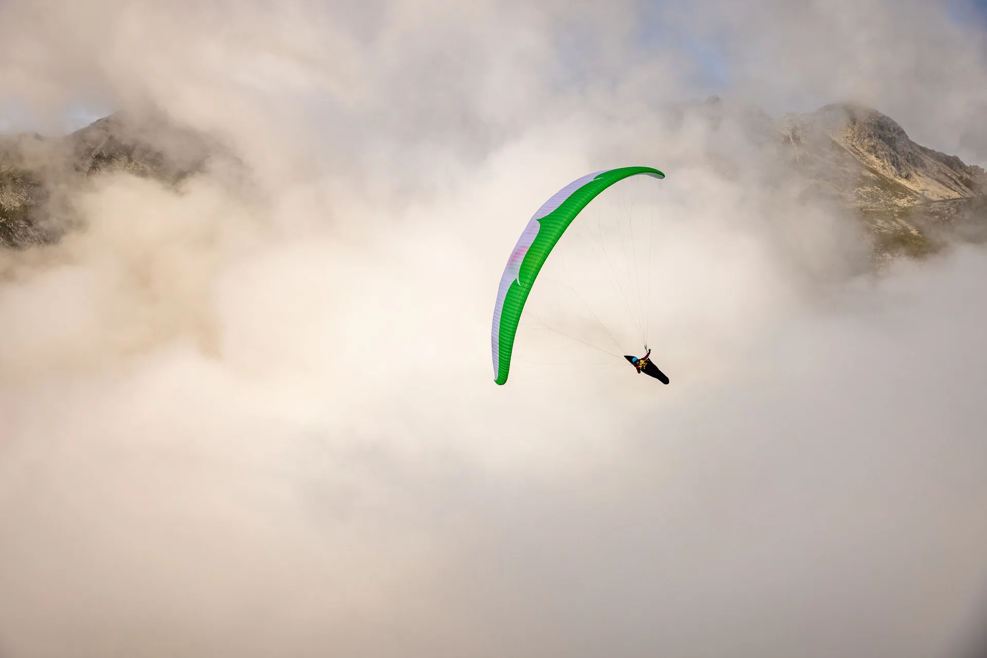 Klaudia Bulgakow fliegt mit ihrem grünen Gleitschirm vor Felswänden und Nebel am Nebelhorn.