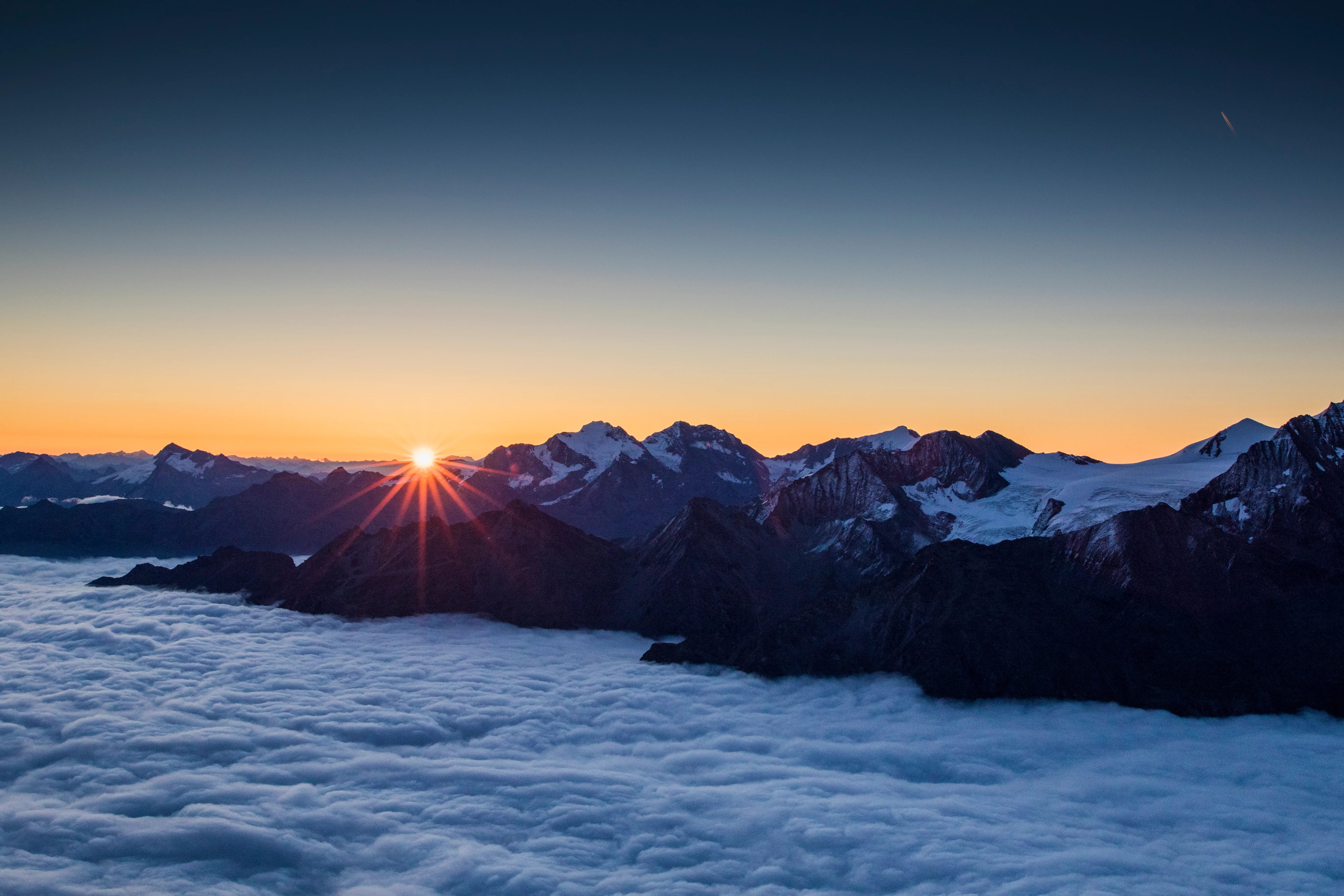 Die Sonne steigt über ein Wolkenmeer zwischen den hochalpinen Gipfeln des Wallis.