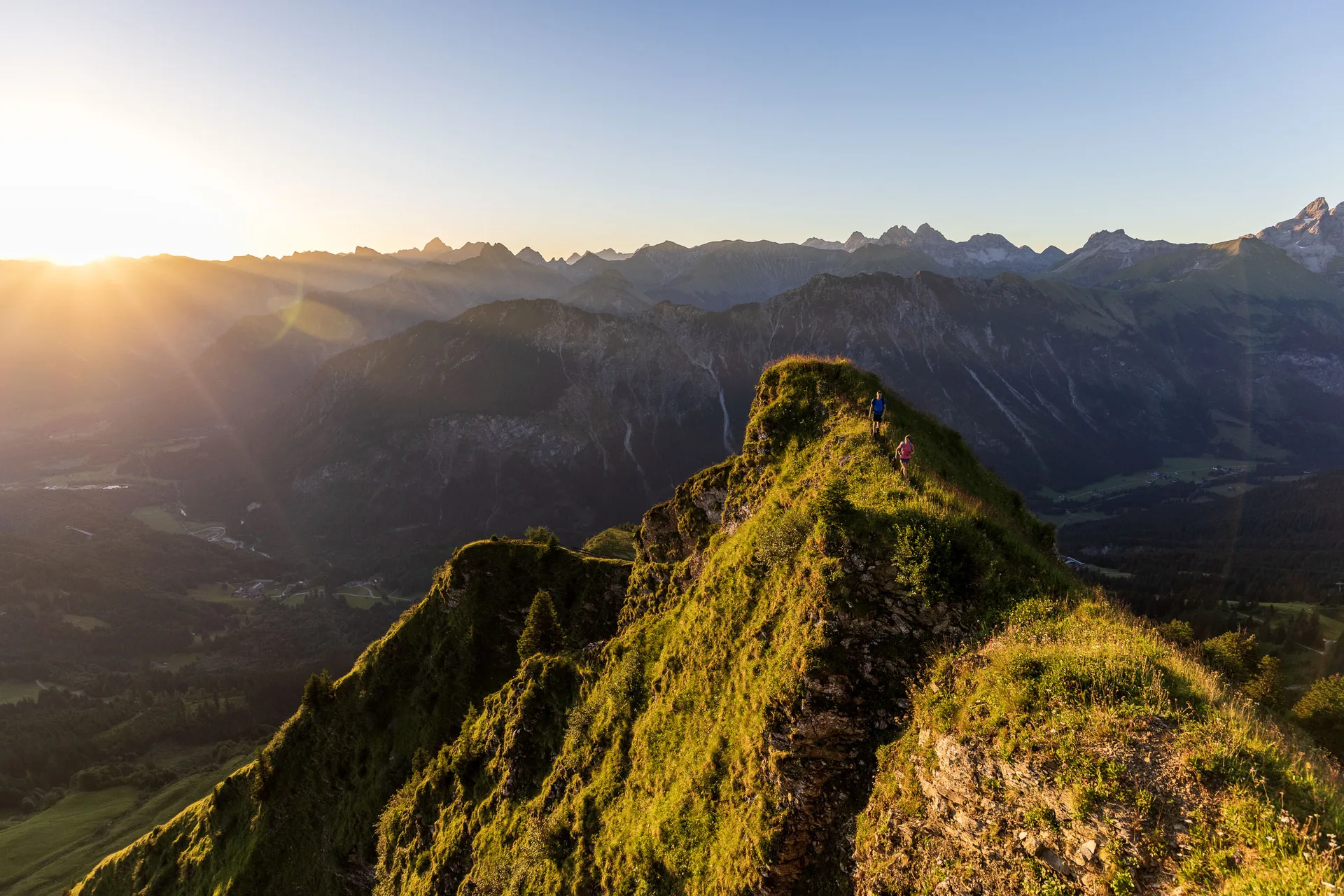 Ein sonniger Gratweg bei Oberstdorf zieht von rechts ins Bild, links fällt der Blick in ein schattiges Tal.