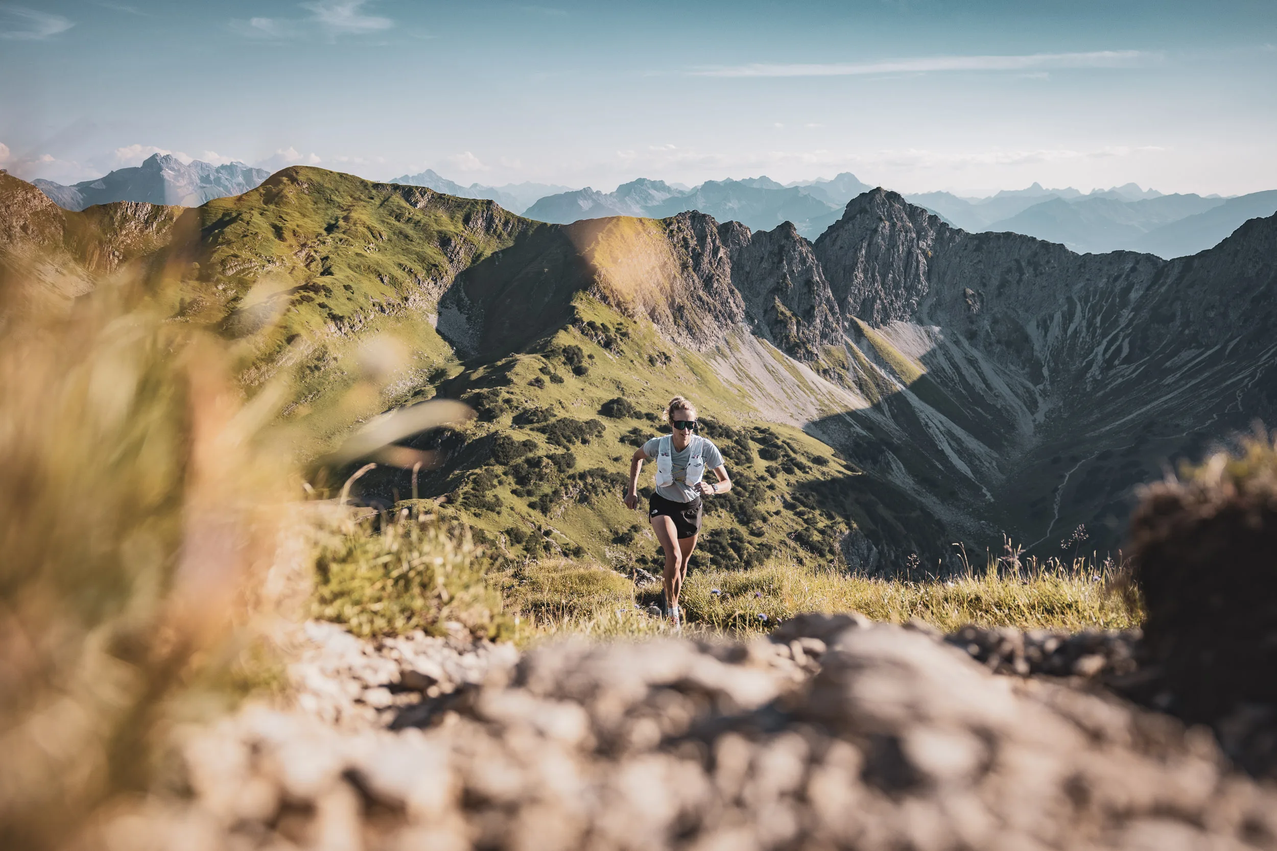 Trailrunnerin auf einem schmalen Bergpfad zwischen Felsen und alpinem Gras