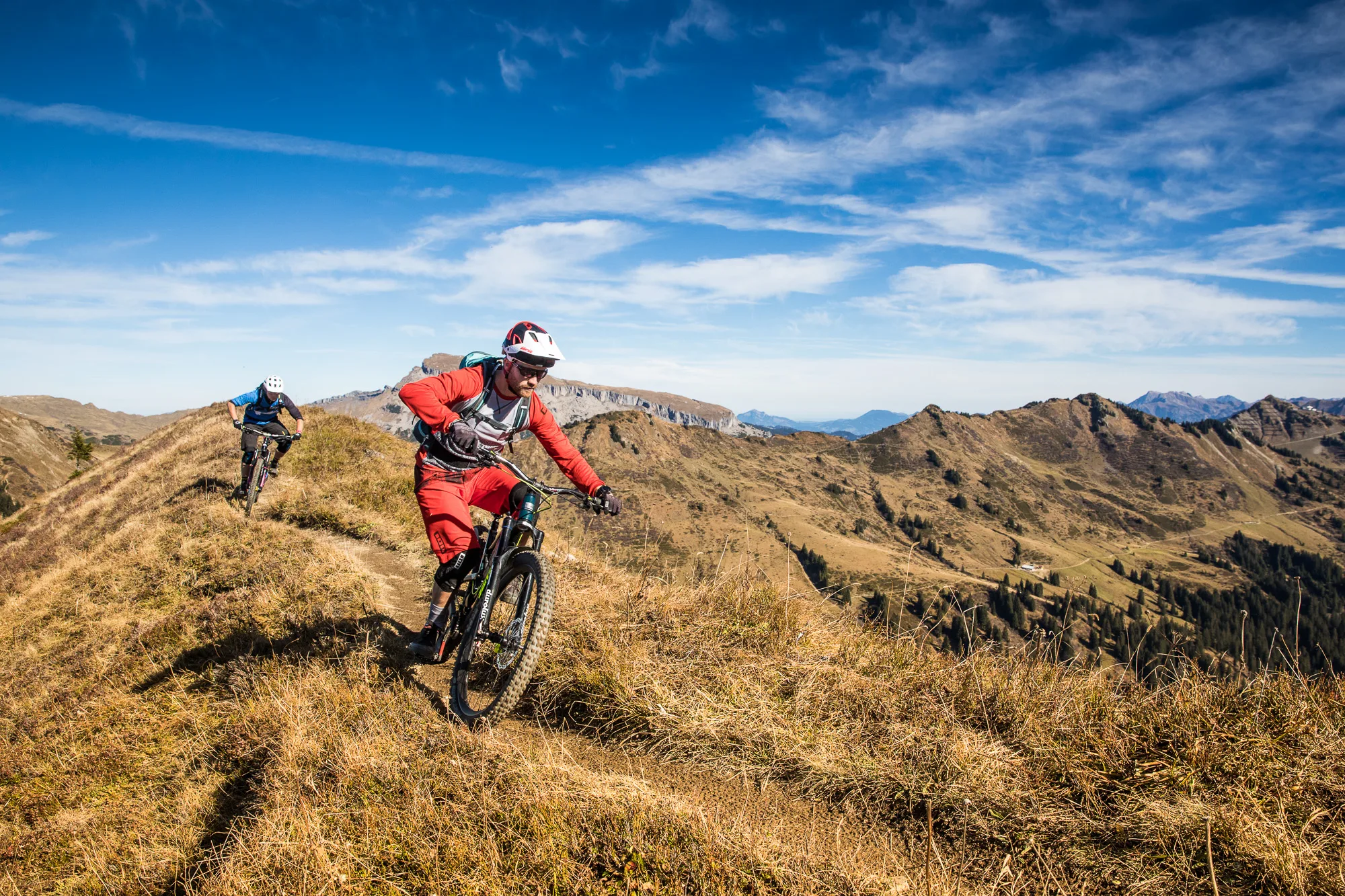 Enduro-Mountainbiker fährt auf einem trockenen Bergtrail mit weitem Alpenblick