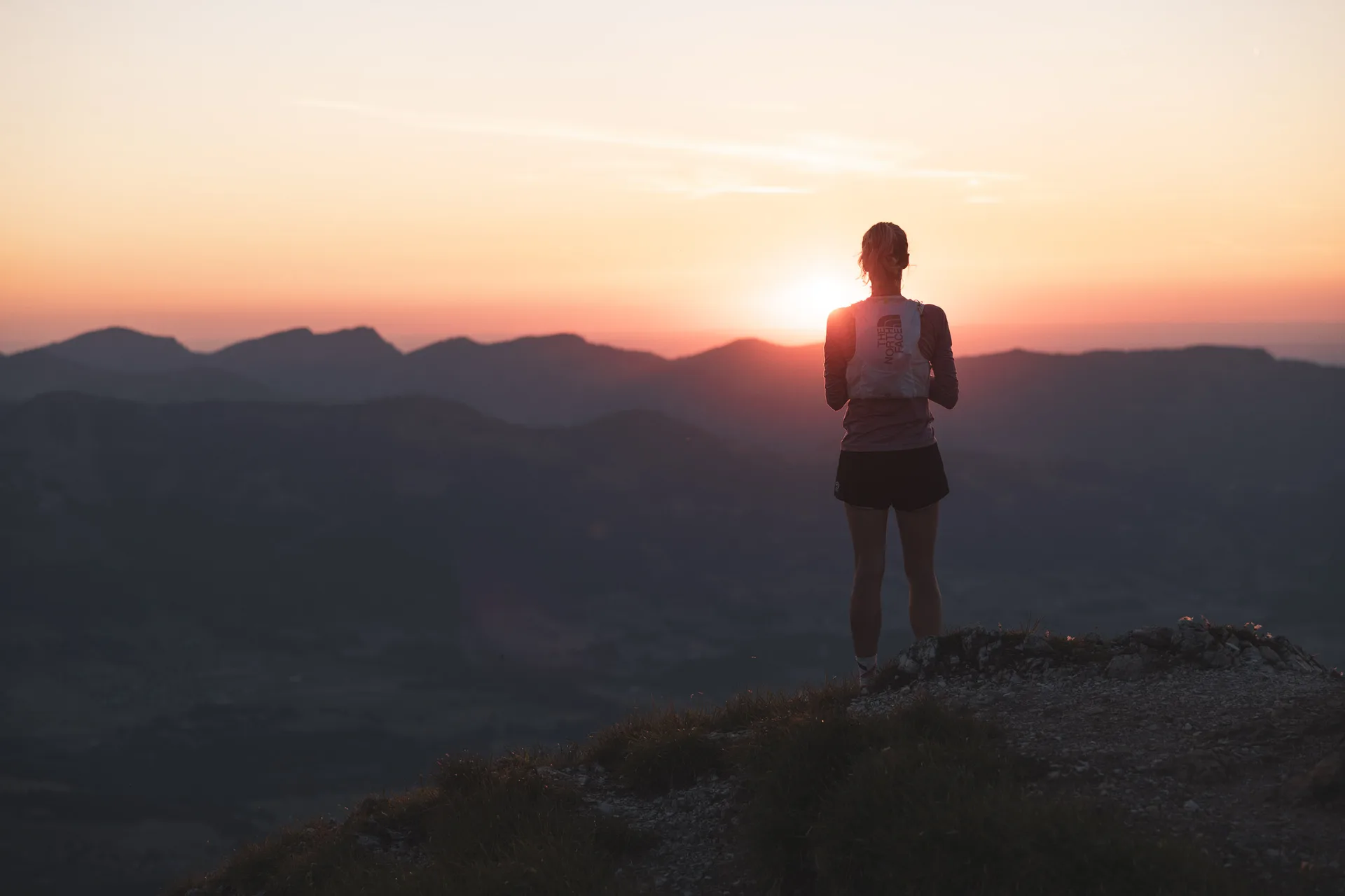 Silhouette einer Trailrunnerin vor der untergehenden Sonne über den Bergen