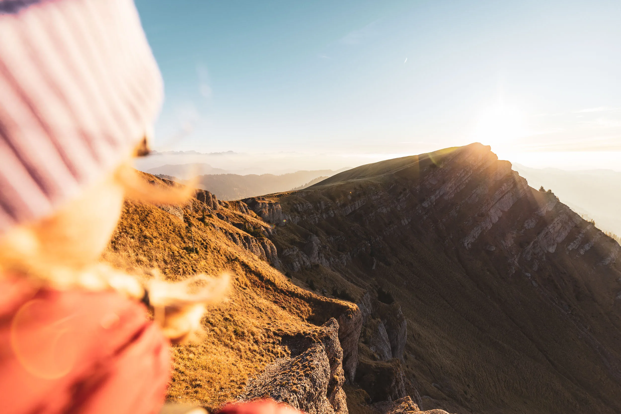Unscharfer Schulterblick einer Wanderin rahmt den hellen Grat im Gegenlicht
