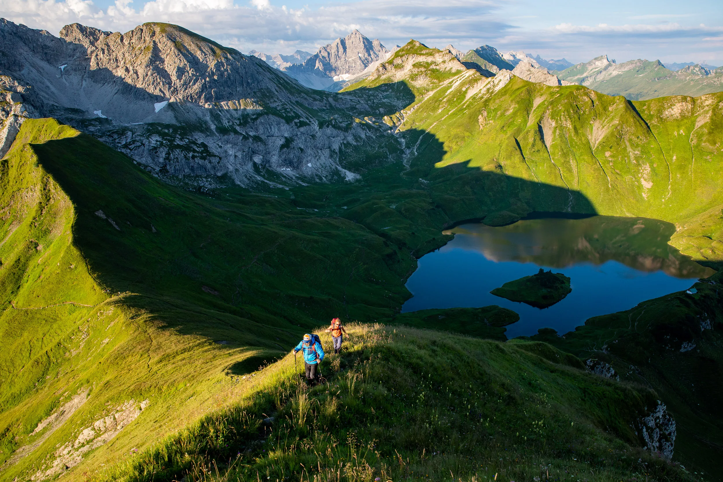 Caroline Nantke und Harald Dreyer wandern auf einem Grasgrat über dem sichtbaren Schrecksee