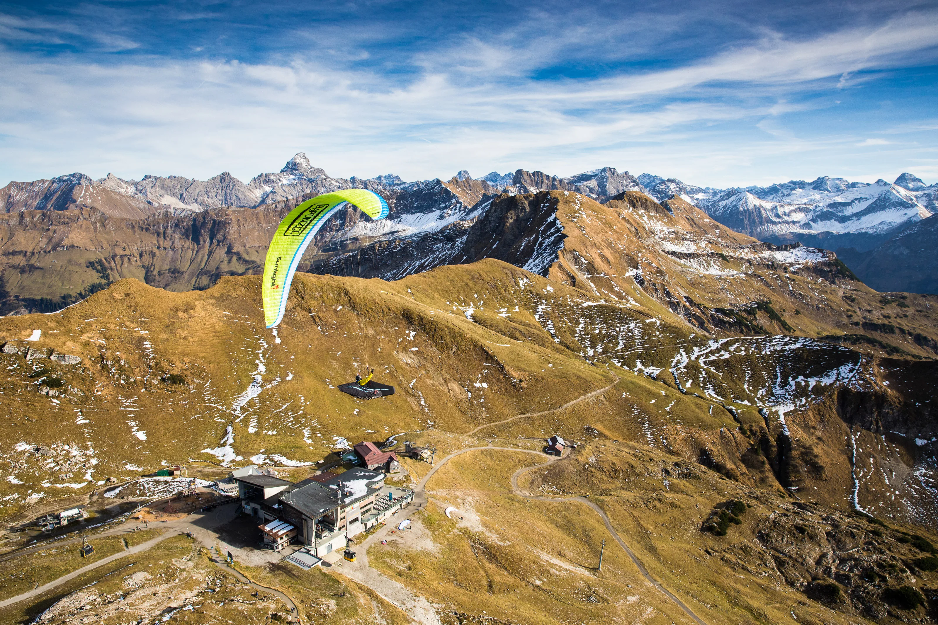 Michael Gebert unter grünem Gleitschirm über dem Nebelhorn mit herbstlichen Bergen und ersten Schneefeldern