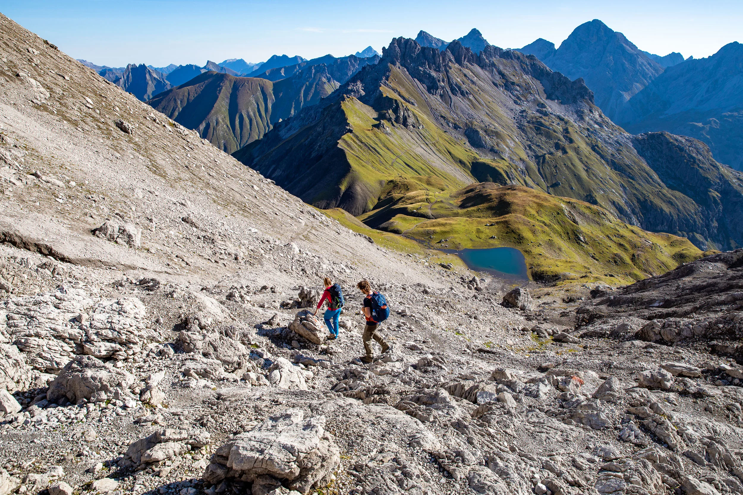 Raphaela Haug und Tom Besser steigen über einen steilen Schutthang mit Blick ins Tal ab