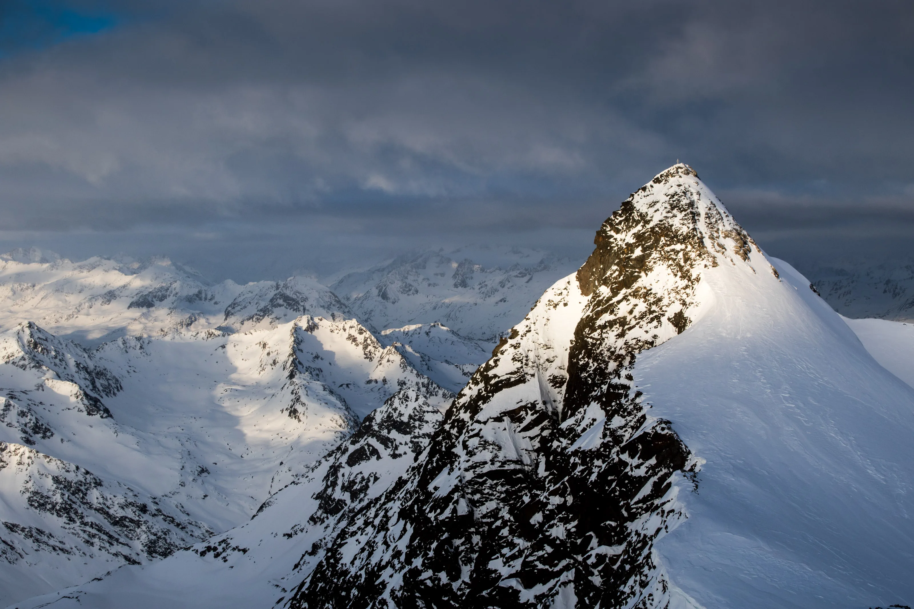 Ein dunkler Felsgipfel erhebt sich zwischen verschneiten Graten über dem Wolkenmeer