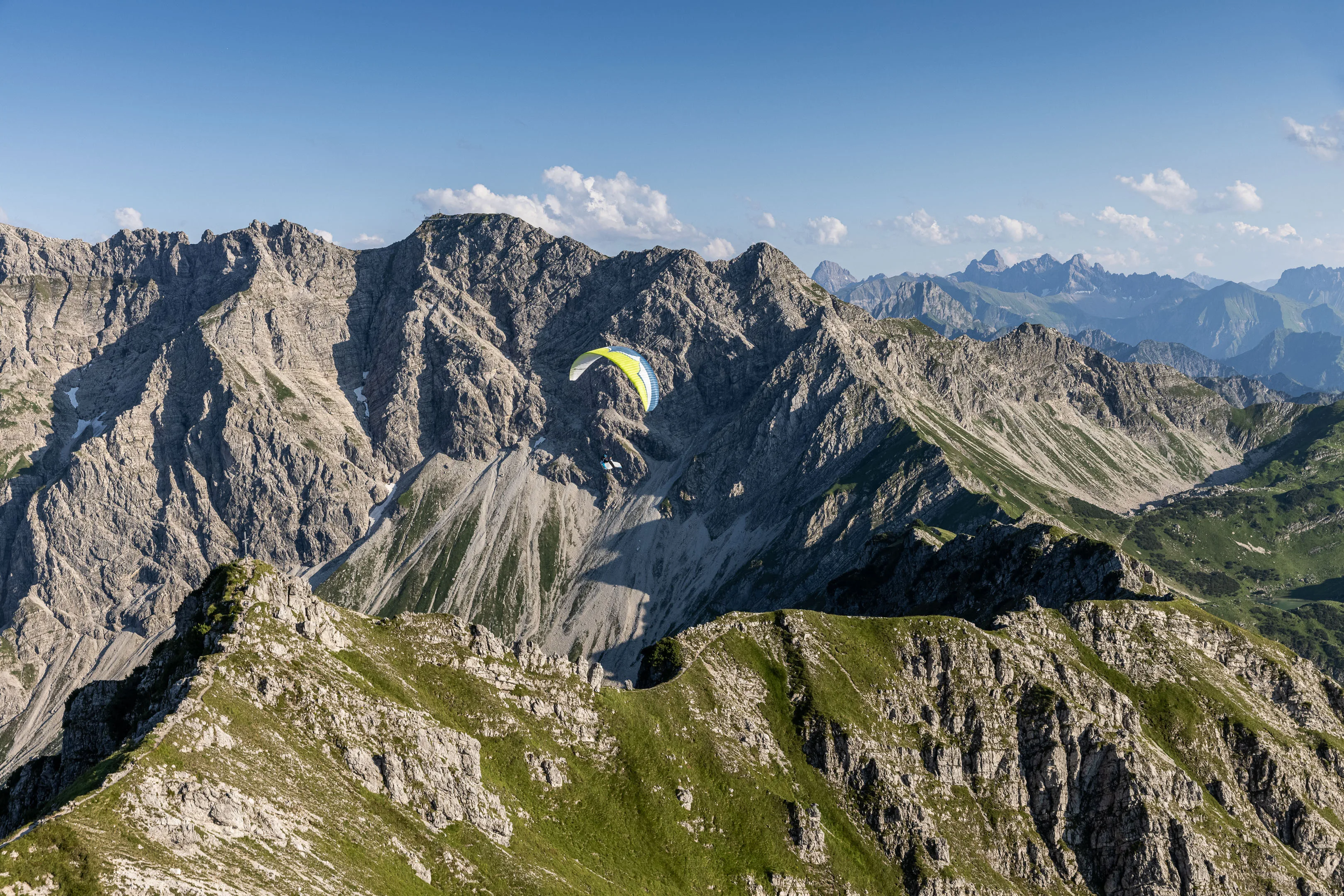 Ein Gleitschirm fliegt durch ein felsiges Hochtal zwischen grauen Kalkwänden