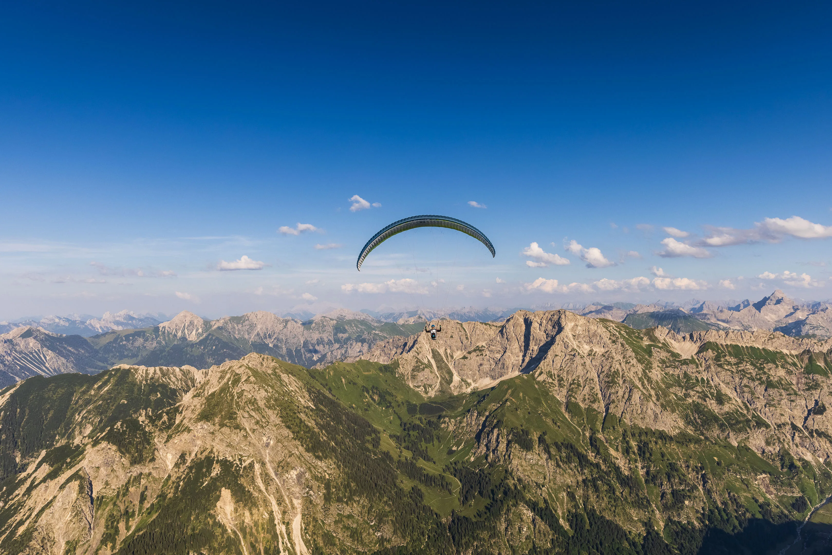 Ein Gleitschirm gleitet mit viel freiem Himmel über die Allgäuer Gipfel