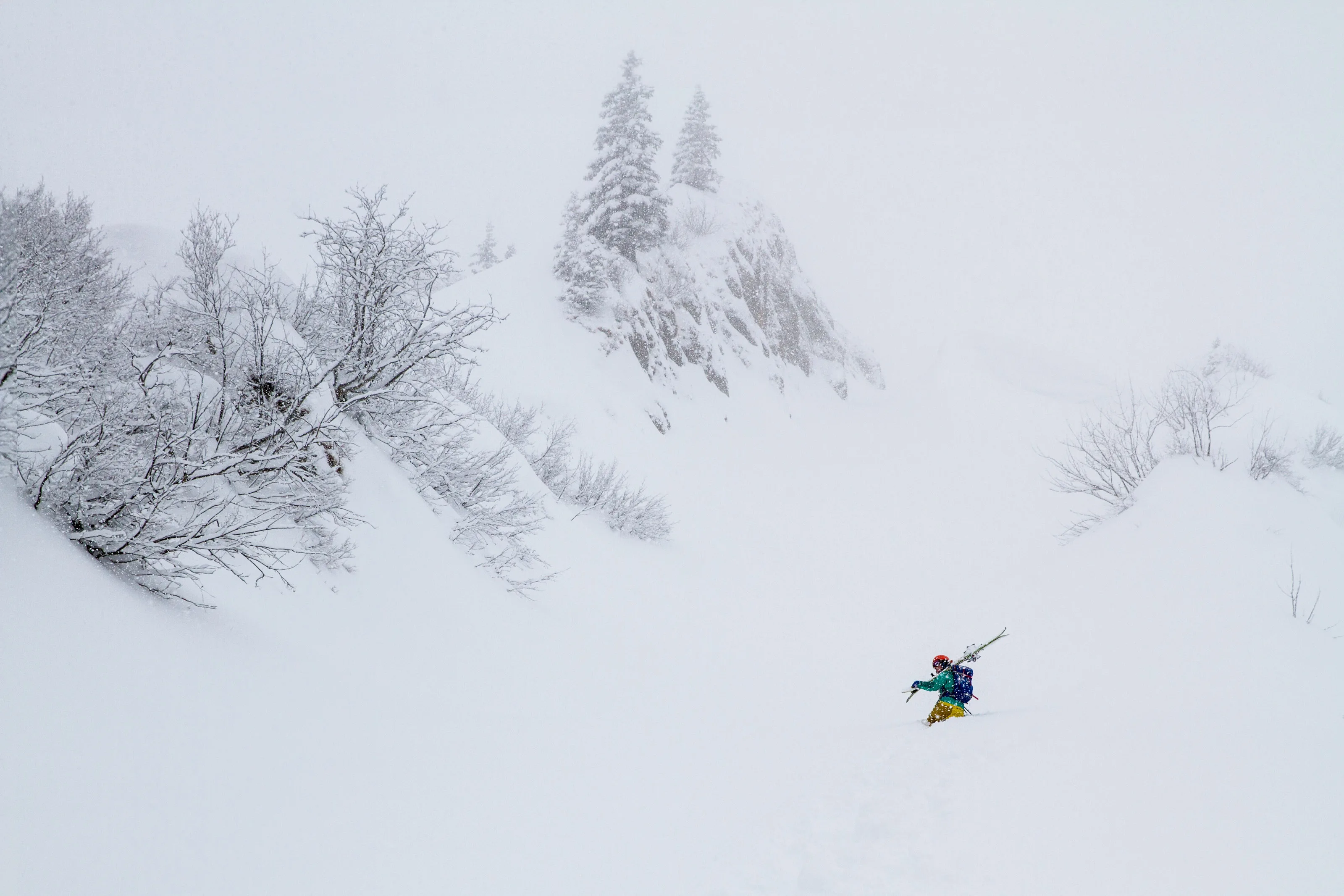 Ein Skitourengeher fährt durch frischen Schnee unter einem nebelverhangenen Felsgrat