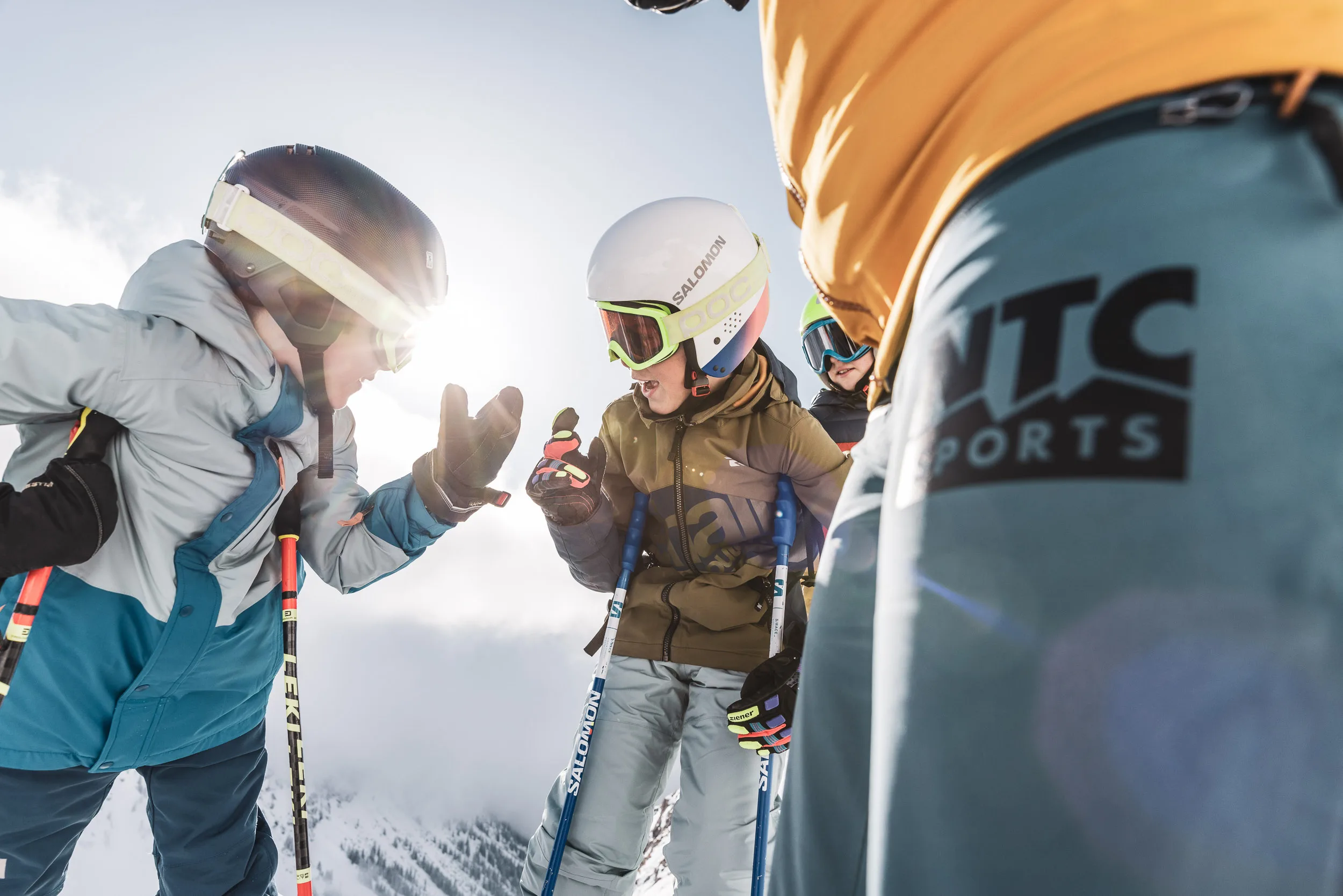 Zwei Kinder geben sich neben einem Skilehrer auf der Piste ein High Five