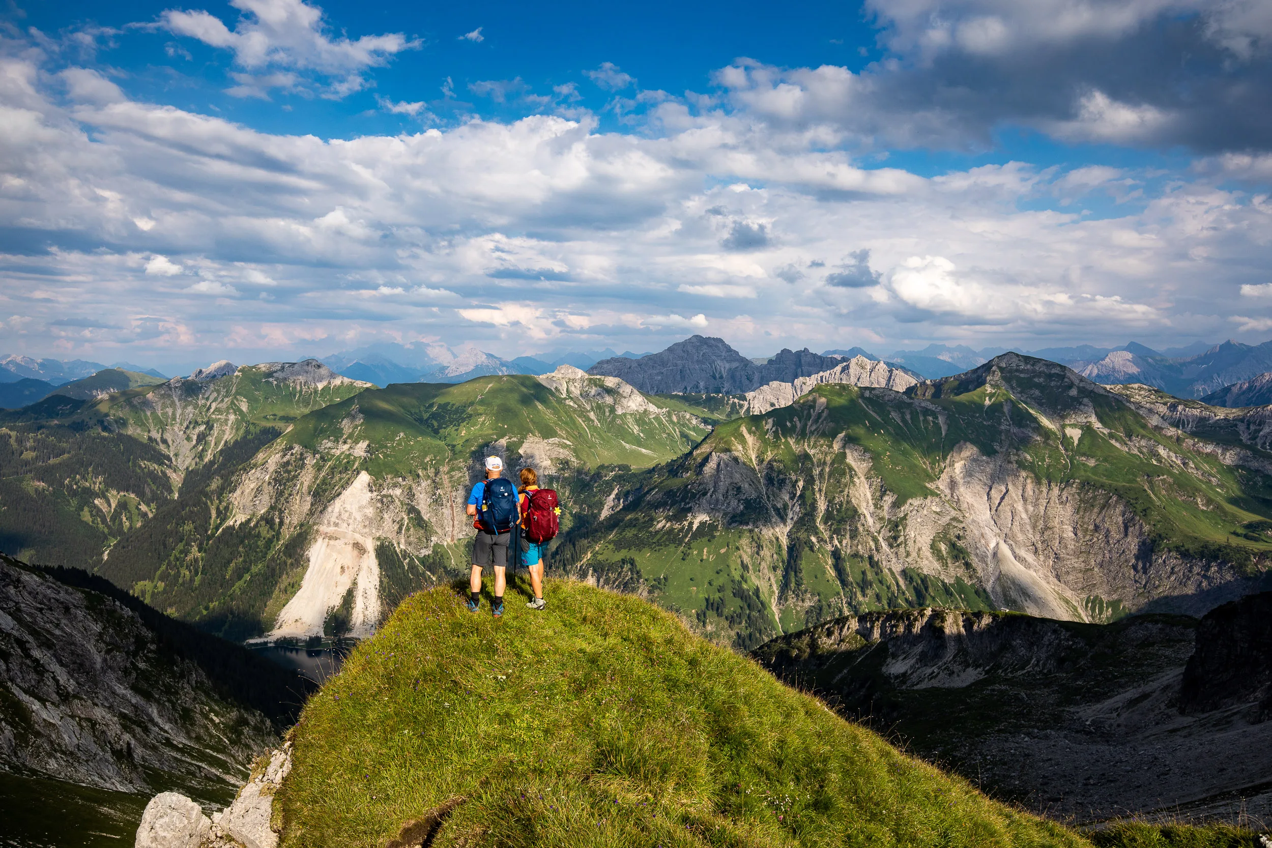 Caroline Nantke und Harald Dreyer stehen auf einer grünen Kuppe vor einer weiten Bergkulisse