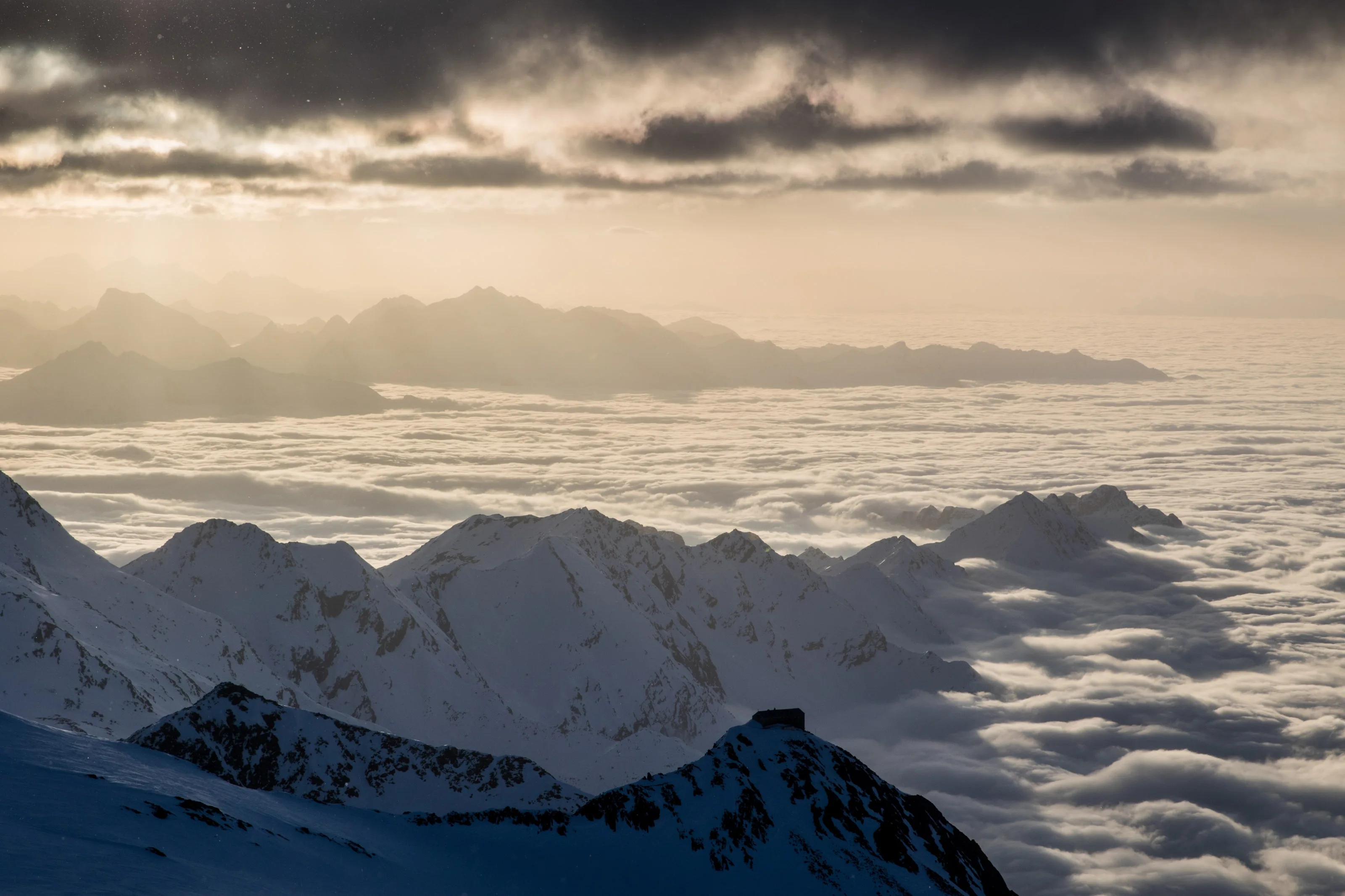 Verschneite Gipfel ragen über ein dichtes Wolkenmeer am Stubaier Gletscher