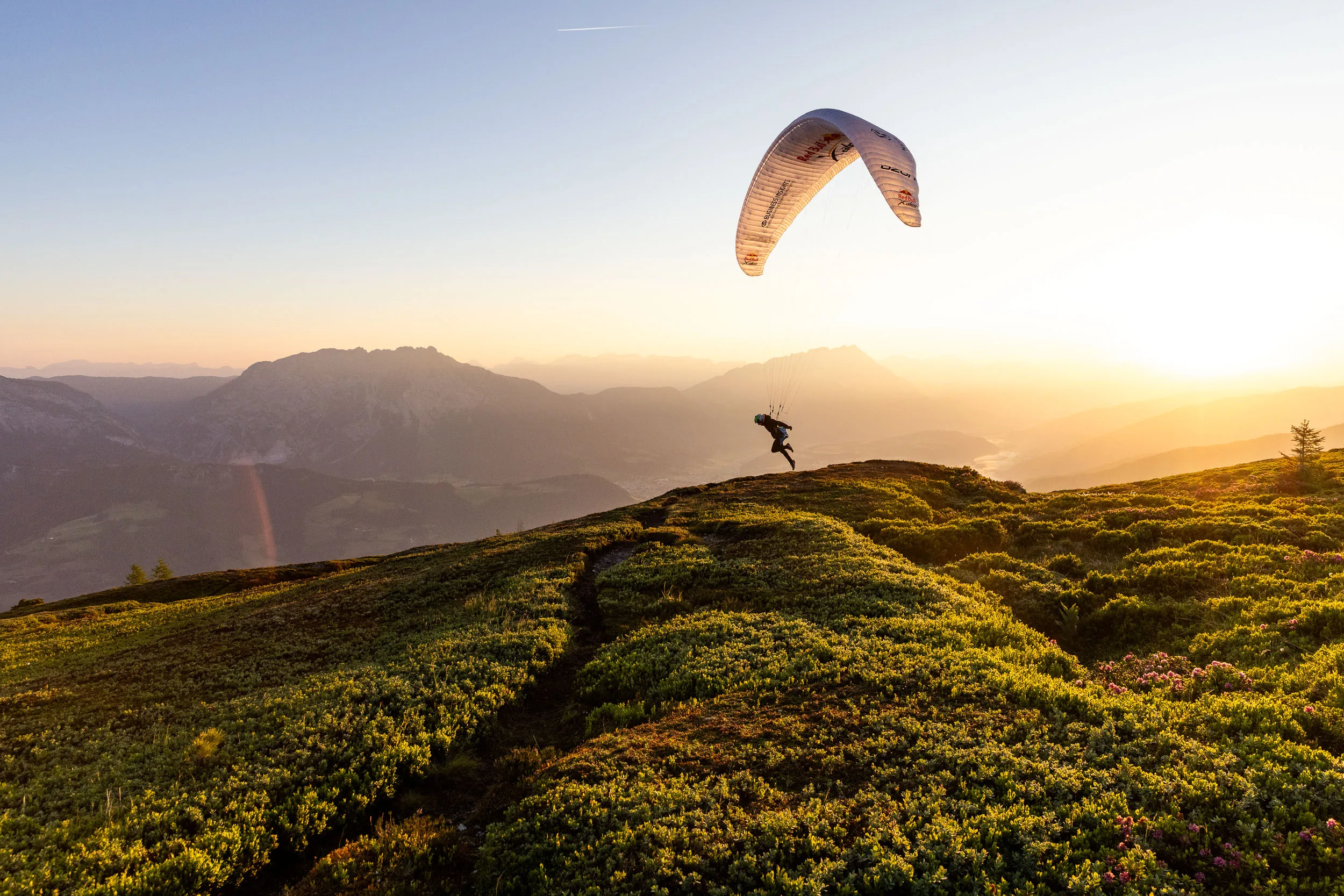 Gleitschirmpilotin hebt mit ihrem Schirm an einem sonnigen Bergruecken ab