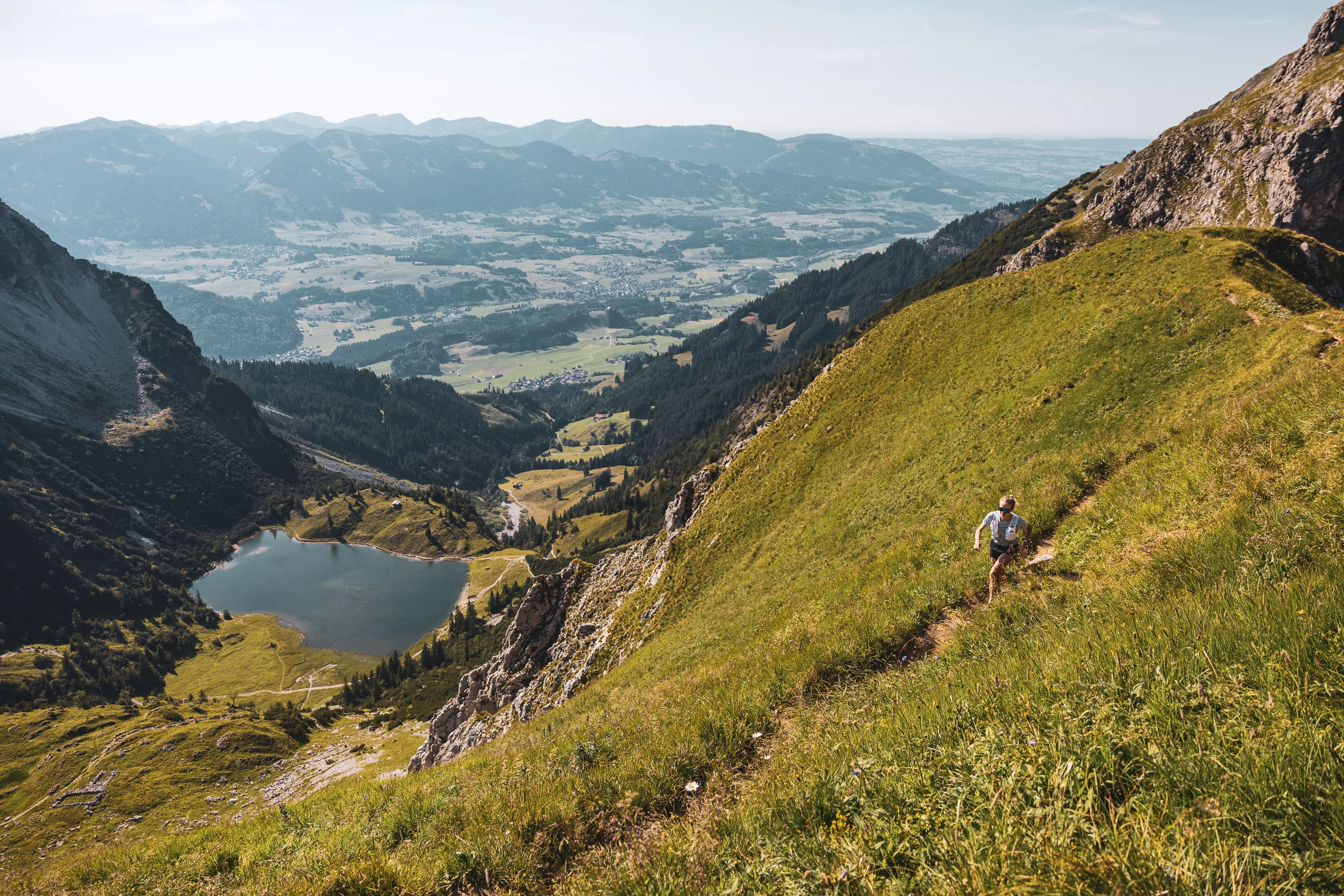 Ronja Morell läuft oberhalb eines Bergsees auf einem steilen Trail mit Blick ins Allgäu