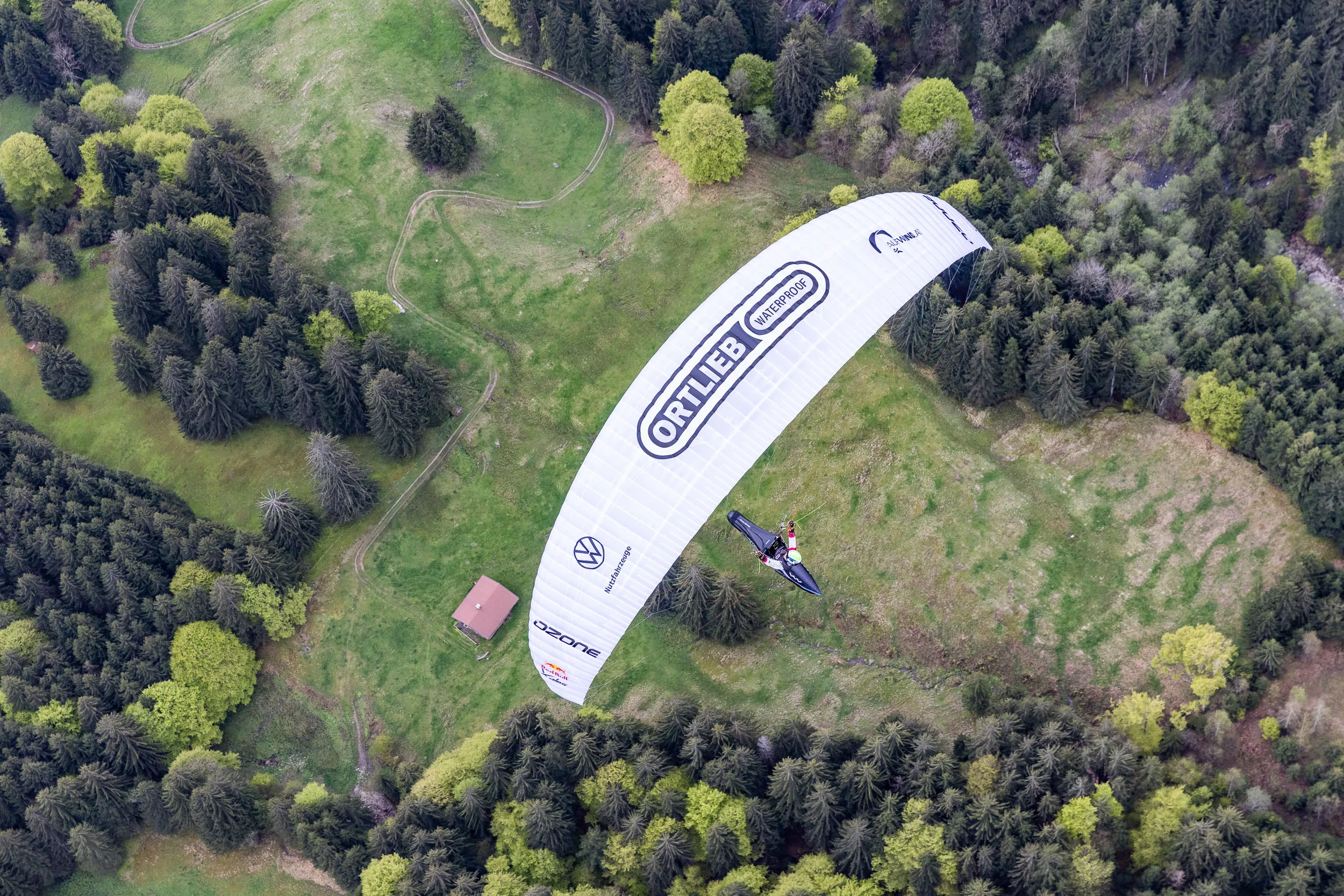 Eli Egger fliegt mit Gleitschirm ueber einer Waldlichtung im Allgaeu.