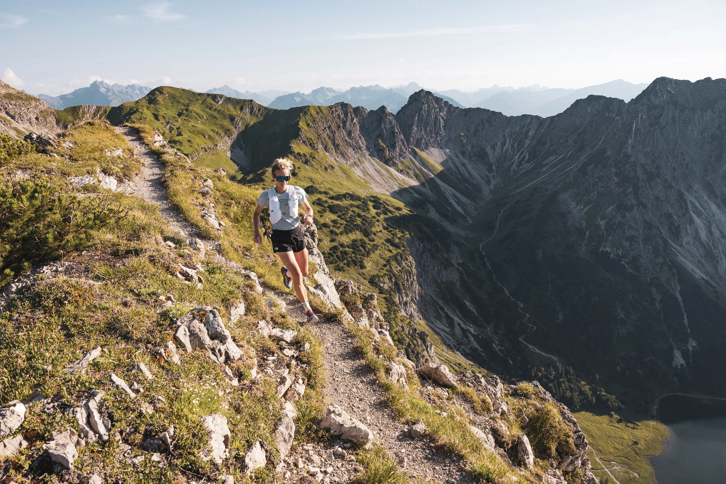 Trailrunnerin auf einem steinigen Bergpfad vor weitem Alpenpanorama